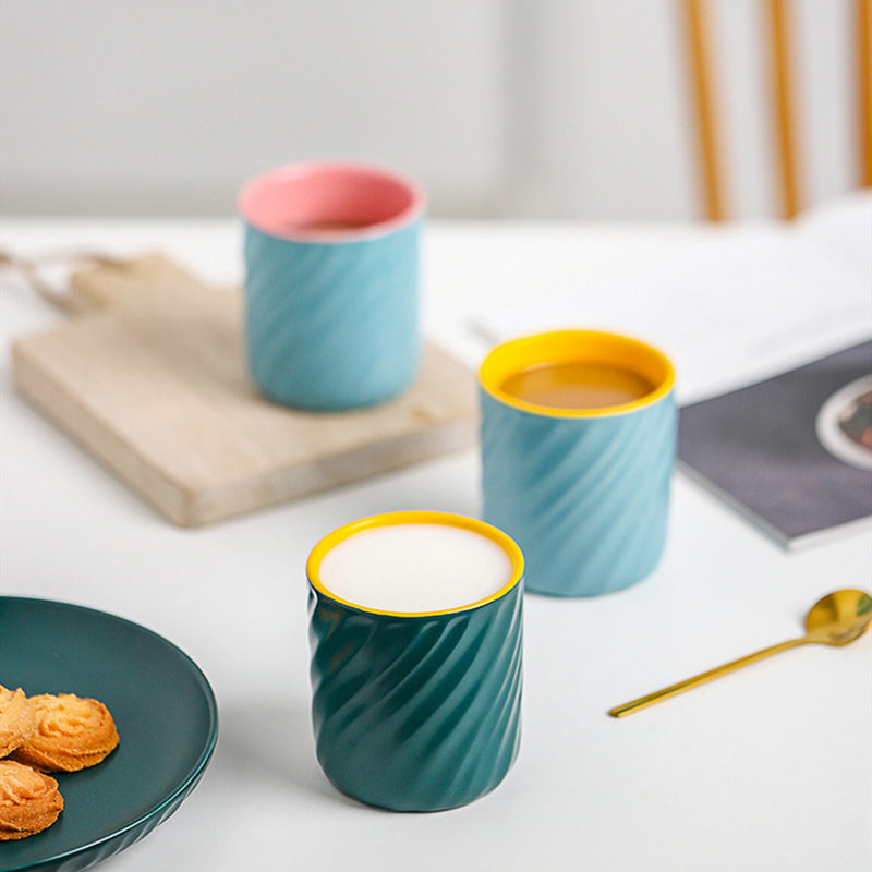 3 Sweet Swirl Cups on a table together. The blue&yellow and blue & pink mugs both have coffee in them, and the green& yellow mug has milk in it. There is a place of cookies on the left beside the green & yellow mug. And a golden spoon on the right of it. 