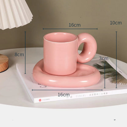 Fun and Bubbly Mug and Saucer Set in pink on top of a book, on top on a table. There is a lamp shade on the top left of the photo. There are product dimensions shown on the photograph.