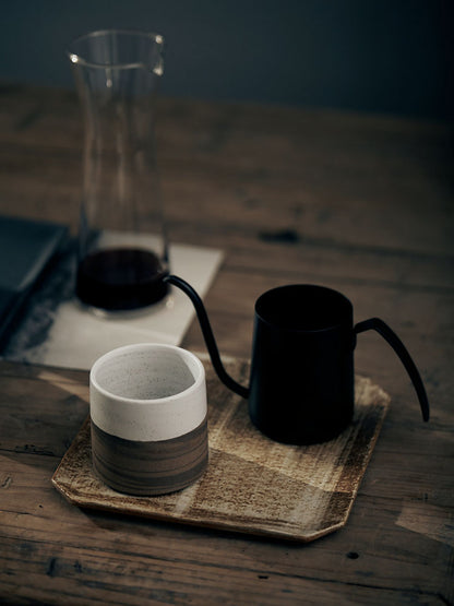 Two-Toned Modern Japanese Style Tea Cup pictured with a kettle and Tall glass of tea in the background.