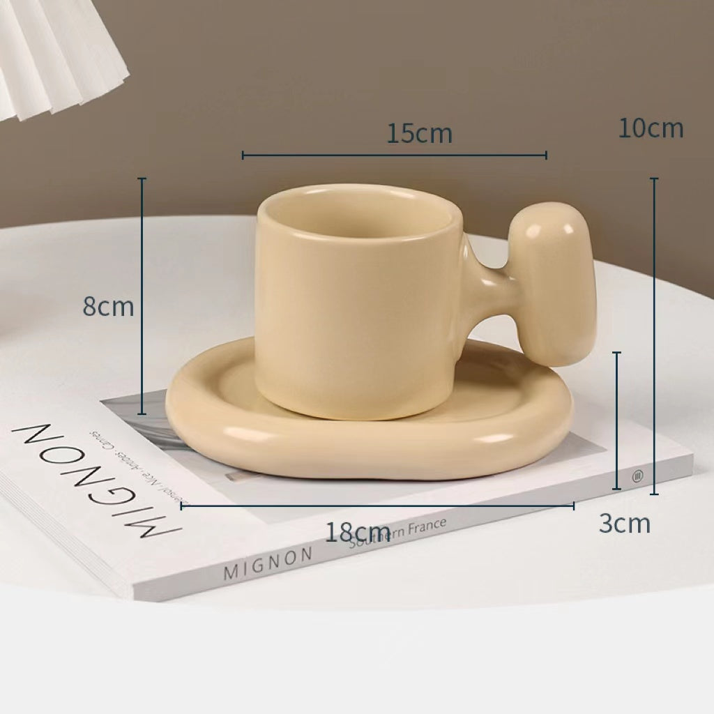 Fun and Bubbly Mug and Saucer Set in beige on top of a book, on top on a table. There is a lamp shade on the top left of the photo. There are product dimensions shown on the photograph.