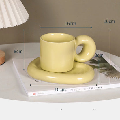 Fun and Bubbly Mug and Saucer Set in muted yellow on top of a book, on top on a table. There is a lamp shade on the top left of the photo. There are product dimensions shown on the photograph.