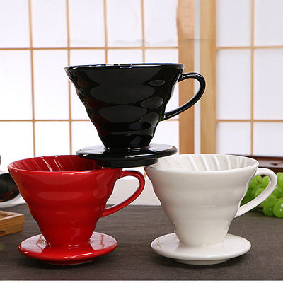 Three Ceramic Pour Over Coffee Filters stacked on top of each other. On the bottom right there is a red ceramic filter and beside it is a white ceramic coffee filter. On the top center of the two ceramic coffee filters, is a black coffee filter, forming a triangle shape.