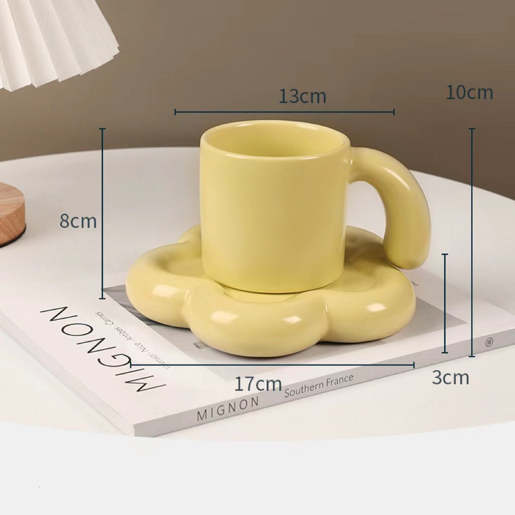 Fun and Bubbly Mug and Saucer Set in muted yellow on top of a book, on top on a table. There is a lamp shade on the top left of the photo. There are product dimensions shown on the photograph.