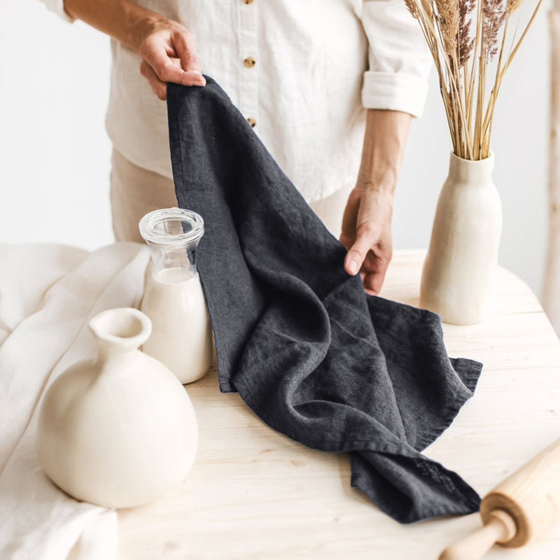 Linen Tea Towel on Table with woman, jar of milk, and ceramic jug, and vase with dried flowers on the table.