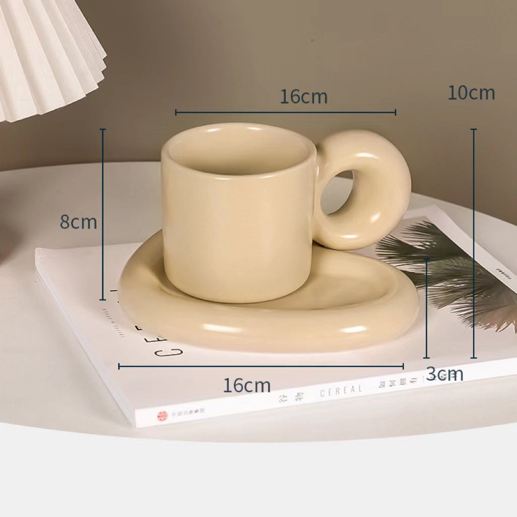 Fun and Bubbly Mug and Saucer Set in beige on top of a book, on top on a table. There is a lamp shade on the top left of the photo. There are product dimensions shown on the photograph.