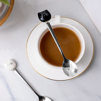 Pet Handle Spoons, one on  the table and one on top of a cup of coffee, on a saucer. All on top of a white table.