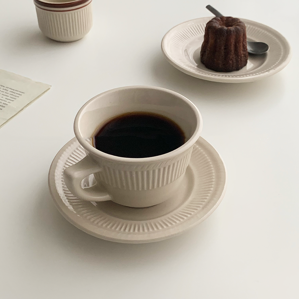 1 coffee cup and 1 coffee cup and saucer set. One is in Cappuccino Brown color and the other is in French Vanilla color. There is another plate with bread pudding on it.