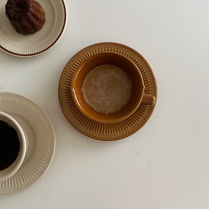 2 coffee cup and saucer sets . One is in Cappuccino Brown color and the other is in White Sugar color. There is another plate with bread pudding on it.