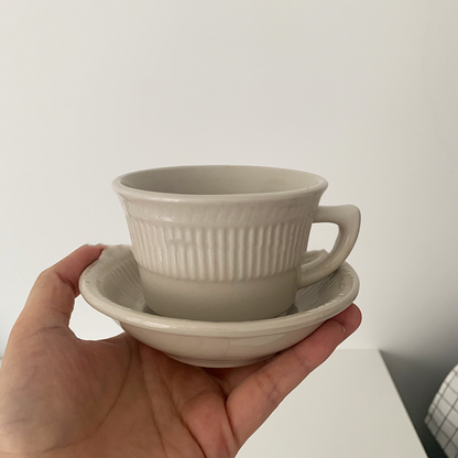 A hand holding a white ceramic mug and saucer