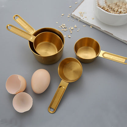 Stainless Steel Measuring Cups and Spoons Set with Removable Rings - 8pcs on a table with an egg, egg shells, and a bowl of oats. Some of the oats are also on the table.