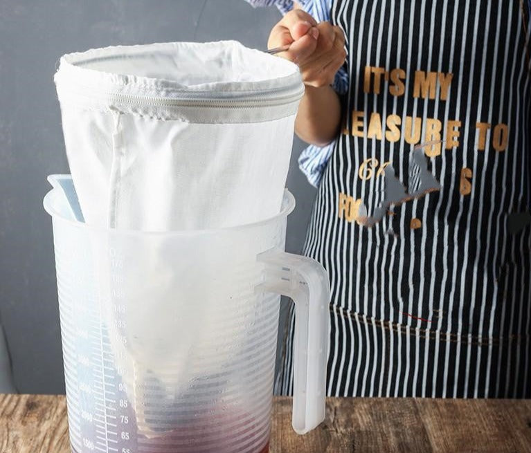 A person holding a Cold Brew Cloth Coffee Filter Brewing Net with coffee in it, into a large clear plastic jug.