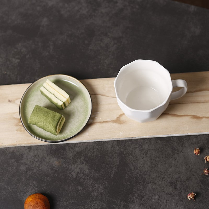 White Diamond-Shaped Ceramic Mug and matcha tea cake on a plate, both on a wooden plank on a table.