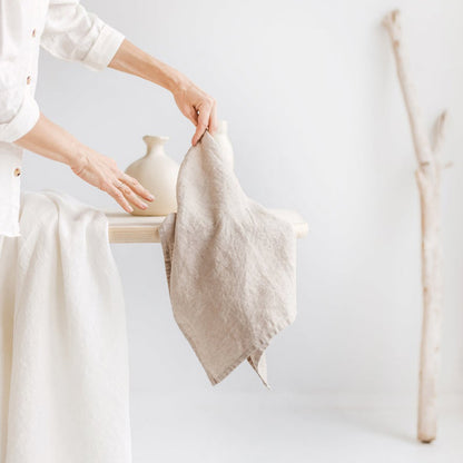 Woman's hands holding Linen Tea Towel on table with two vases and another piece of cloth.